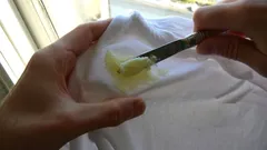 Máslo na bílé látce, odstraňování mastného fleku pomocí nože.
