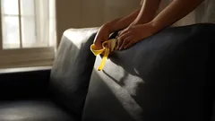 Čištění kožené pohovky žlutým hadrem v slunečně osvětleném obývacím pokoji.