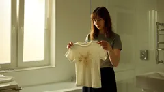 Žena drží zašpiněné tričko v prádelně u okna, kontrola skvrn na oblečení.