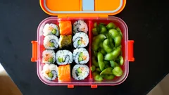 Krabička sushi a edamame fazolí na černém stole, zdravý oběd v boxu.