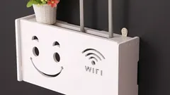 Bílý kryt na Wi-Fi router s usměvavým obličejem a symbolem Wi-Fi, květináč nahoře.