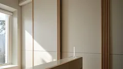 Moderní minimalistický interiér s bílými stěnami, dřevěnými prvky a slunečním světlem z okna