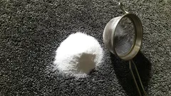Hromádka cukru a nerezové sítko na tmavém podkladu