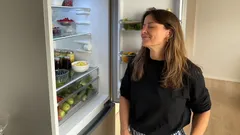 Žena stojí u otevřené lednice a vybírá jídlo v moderní kuchyni.